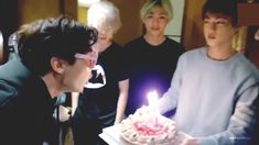 a group of people standing around a cake with a lit candle on top of it