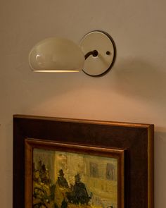 a painting is hanging on the wall next to a light fixture that has been turned on