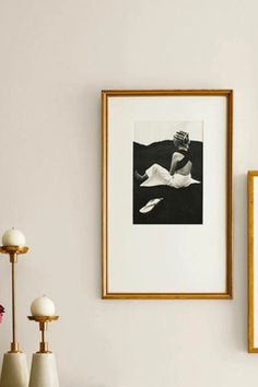 two framed photographs hang on the wall next to vases with flowers and lamps in them