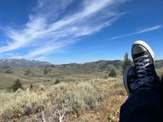 a person's feet in the grass with mountains in the background and blue sky