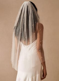the back of a bride's veil with white pearls on it and her dress