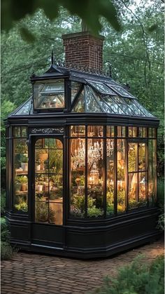 A black corner greenhouse with glass walls featuring plants and a chandelier glowing inside.