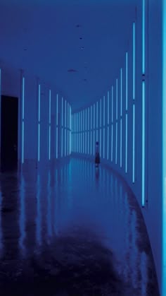 an empty hallway with blue lights on the walls and dark flooring in front of it