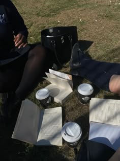 two people sitting on the grass with open books and coffee cups in front of them