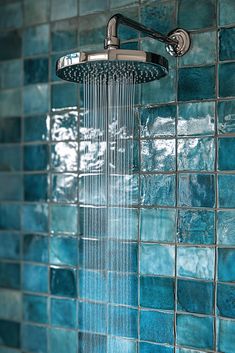 a shower head with blue tiles on the wall and water running down it's side