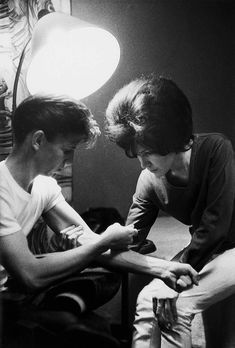 two young men sitting next to each other in front of a lamp and looking at their cell phones