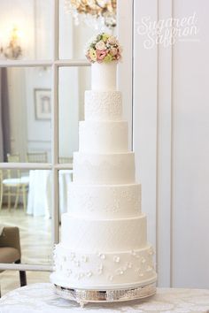a white wedding cake sitting on top of a table next to a glass window with a chandelier hanging from it