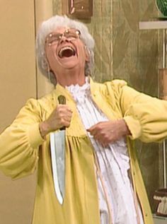 an older woman holding a knife and singing into a microphone in front of a mirror