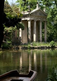 a boat sitting on the water in front of a building with columns and trees around it
