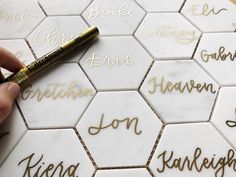 someone is writing on some white tiles with gold lettering and a pen in their hand