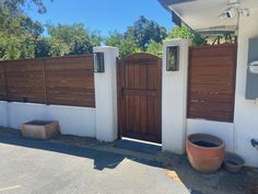 two large planters sitting outside of a white house with wooden gates on the side