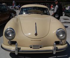 an old beige car parked in a parking lot next to other cars and people walking around
