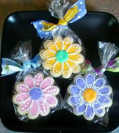 three decorated cookies sitting on top of a black tray next to plastic bags with bows