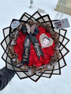 someone is holding a valentine's day wreath with roses and hearts on it in the snow