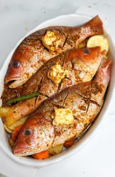 cooked fish in a white dish with lemon wedges