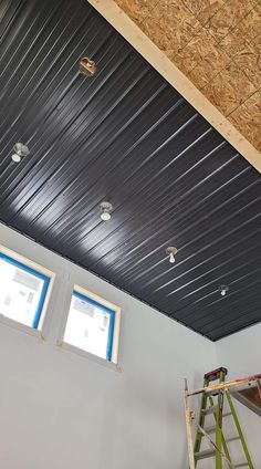 an unfinished room with two windows and a ladder on the wall next to it that is being worked on