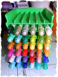 many different colored pens are lined up in a row on top of a paper workbench