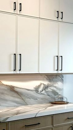 a kitchen with white cabinets and marble counter tops