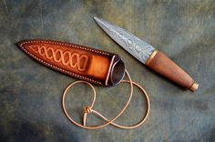 a knife is laying on top of a brown leather case and has a cord attached to it