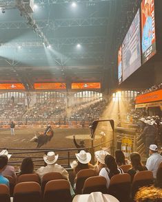 an arena full of people watching a man riding a horse in the air at a rodeo