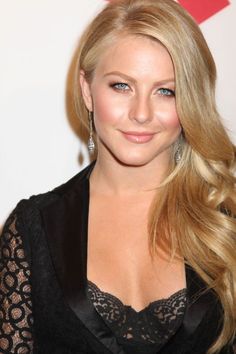 a woman with long blonde hair wearing a black dress and smiling at the camera while standing in front of a wall