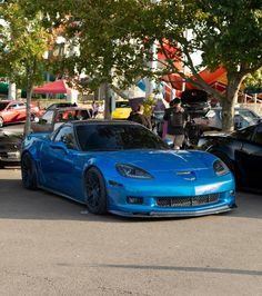 two cars parked next to each other on a parking lot with trees in the background
