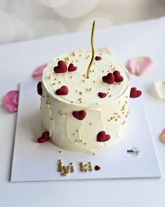 a white cake with red hearts on it and the word love spelled in gold letters