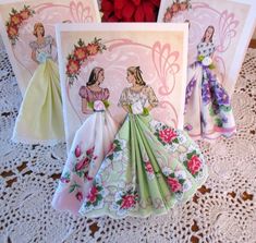 three greeting cards with paper dolls on top of them, one in green and the other in pink