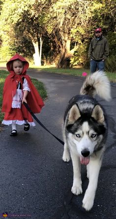 two children are walking their husky dog on a leash in the park, one is wearing a red cape