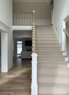 a staircase leading up to a living room and dining room area with white walls, wood flooring and beige carpet