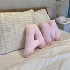 three pink pillows sitting on top of a white bed
