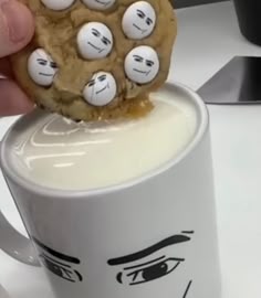 a person holding a cookie in front of a coffee mug with faces drawn on it