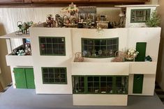 a white doll house with green windows and lots of toys on the top shelf in front of it