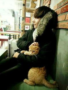 a person sitting on a bench with a cat in their lap and one arm around the other