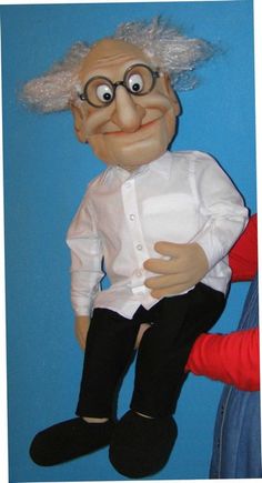 an old man doll sitting on top of a blue wall