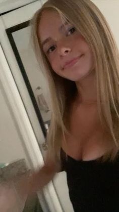 a woman with long blonde hair standing in front of a mirror looking into the camera