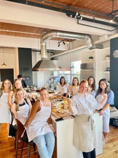 a group of women in aprons standing around a kitchen island with food on it