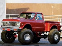 a red truck with big tires parked in front of a building