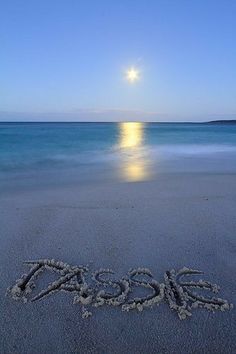 the word oasis written in the sand on a beach at night with the moon rising over the ocean