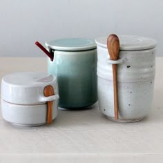 three ceramic jars with wooden spoons in them on a table top next to each other
