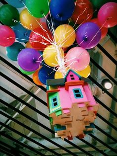 a bunch of balloons floating in the air above a house with a tree on top