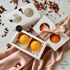 two oranges in a white box on a pink satin tablecloth with rose petals