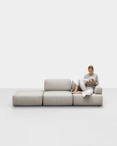 a woman sitting on top of a gray couch next to a white wall and floor
