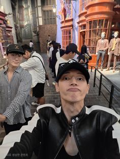 a man wearing a black hat and leather jacket posing for a photo in front of a group of mannequins