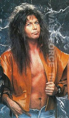 a man with long hair and no shirt standing in front of a black background wearing a leather jacket