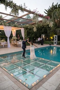 a bride and groom are dancing in front of an outdoor pool at their wedding reception