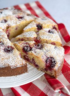 a cake with powdered sugar and berries on it sitting on a red and white checkered table cloth