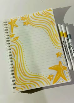 an open notebook with yellow stars and swirls on it, next to two markers