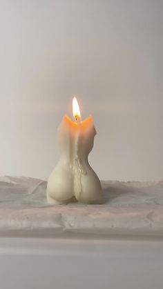 a lit candle sitting on top of a white sheet covered tablecloth next to a wall
