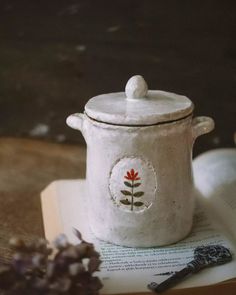 an open book sitting on top of a table next to a white pot with a flower painted on it